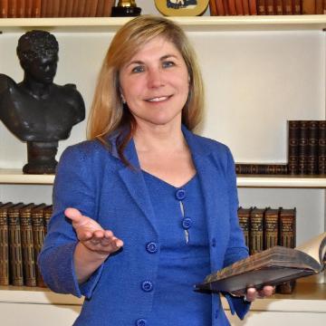 A woman in a blue suit holding a book and gesturing.