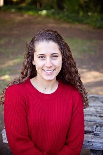A person in a red sweater smiling outdoors.