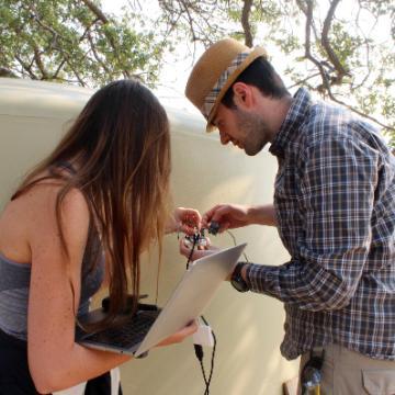 Two people writing or drawing on an outdoor whiteboard.