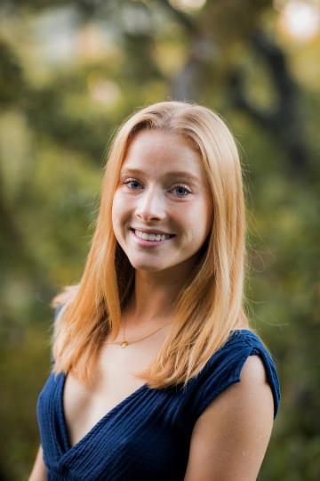 A person wearing a dark blue top, smiling in an outdoor setting.