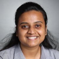 Woman smiling in a headshot against a grey background.