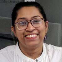 A person smiling, wearing glasses and a white shirt.