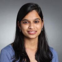 A person smiling in a professional headshot against a grey background.