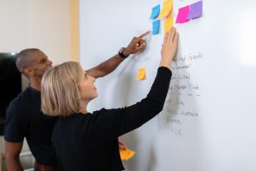 Two people looking at a whiteboard with post-its 
