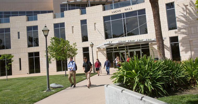 Alt text: People walking near Lucas Hall as seen from Vari Hall on a sunny day.