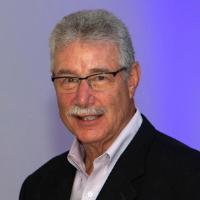 Man in suit with glasses, light mustache, and smiling.