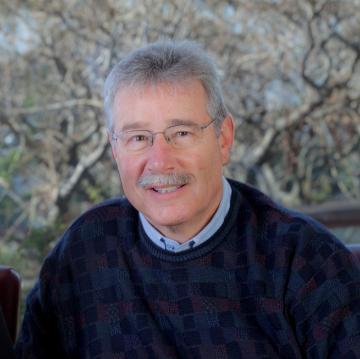 A smiling person seated with a nature background.