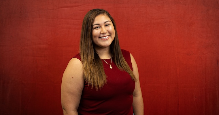 Young woman smiles in front of red backdrop.