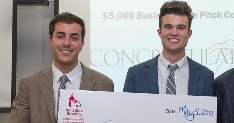 Three men holding a large check in a classroom.