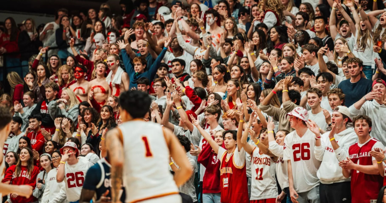 A Broncos player jogs by a large crowd of cheering students at a basketball game