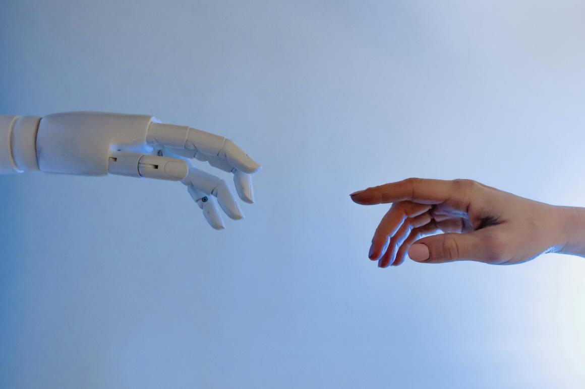 Robotic hand stretched out to touch fingers with human hand