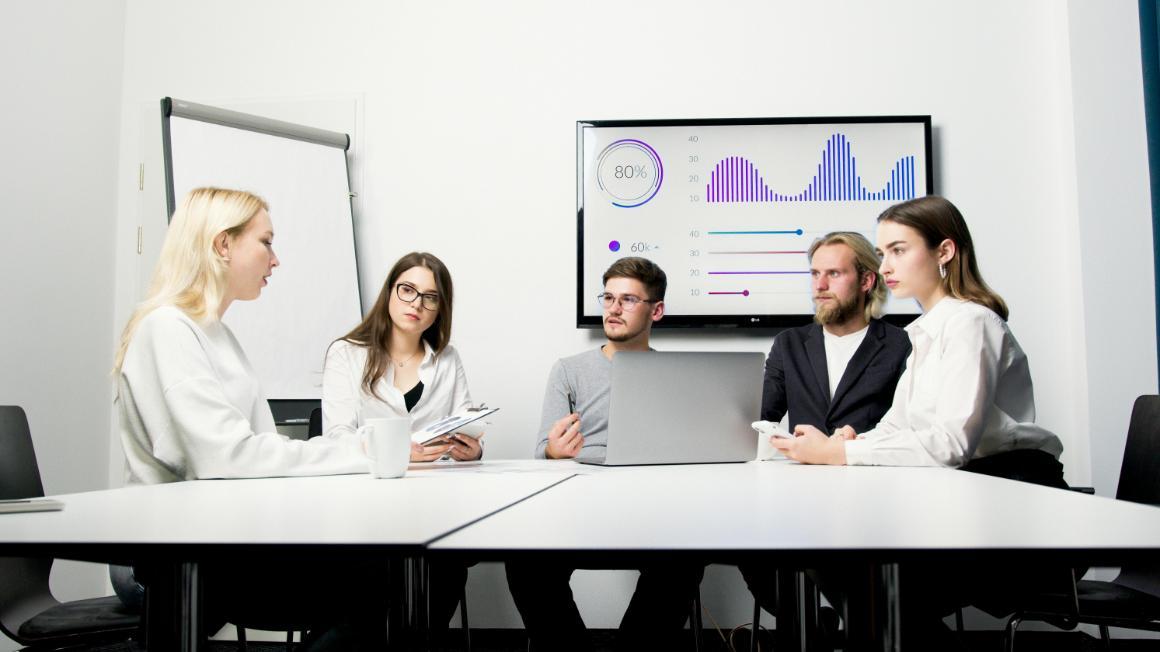 Business professionals in a meeting room with graphs behind them