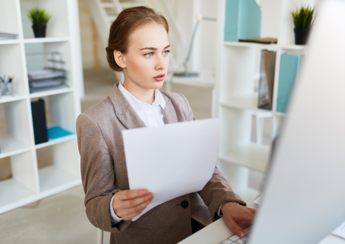 Business woman in suit holding paper while navigating computer