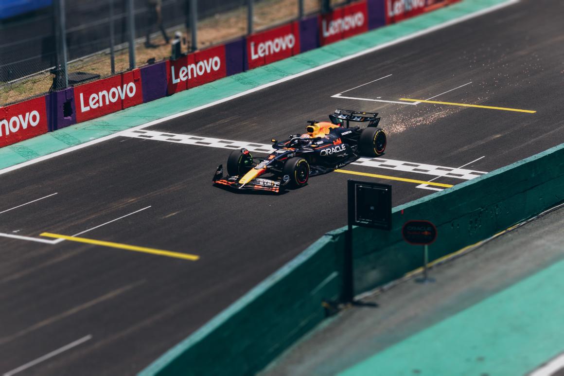 A Formula 1 car crosses the finish line on a racetrack, with Lenovo branding in the background and debris flying from its tires.