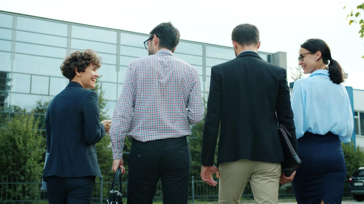 Four adults walk and talk outside a modern glass-fronted building.
