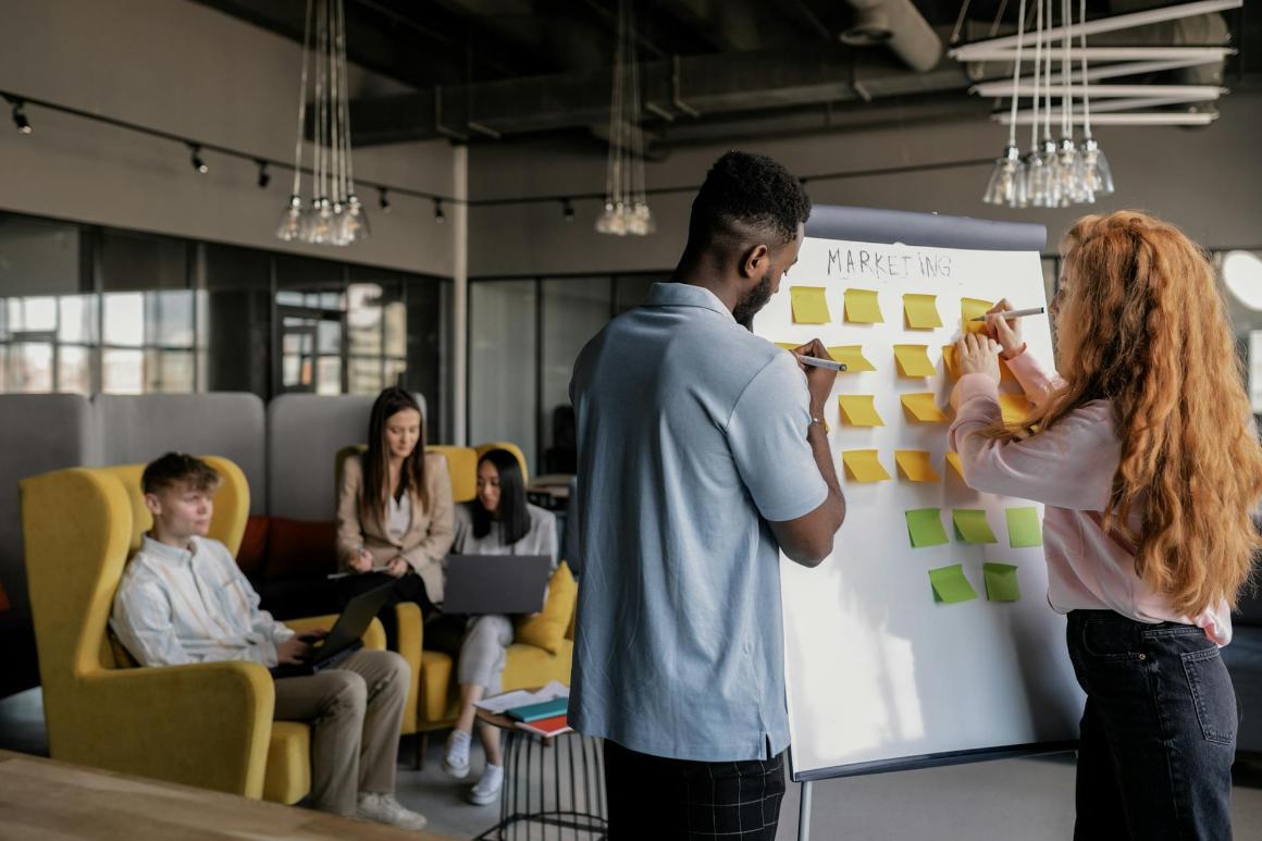 Two individuals are standing at a whiteboard for marketing planning session