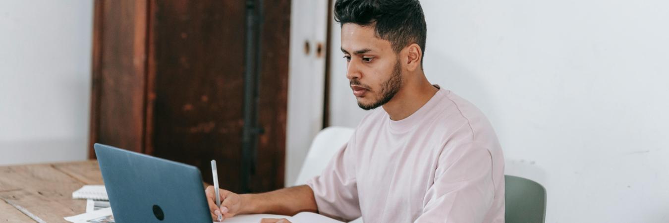 Student working on laptop while taking notes by hand