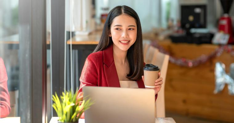 Happy smile young businesswoman in a red suit sitting holding coffee with laptop computer in café