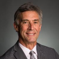 A person in a grey suit standing with crossed arms.