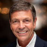 A person smiling in professional attire with a blurred background.