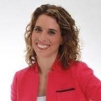A woman in a pink blazer smiling against a white background.