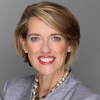 A woman in a grey suit smiling against a grey background.