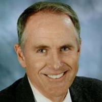 A professionally dressed man smiling with a suit and tie.