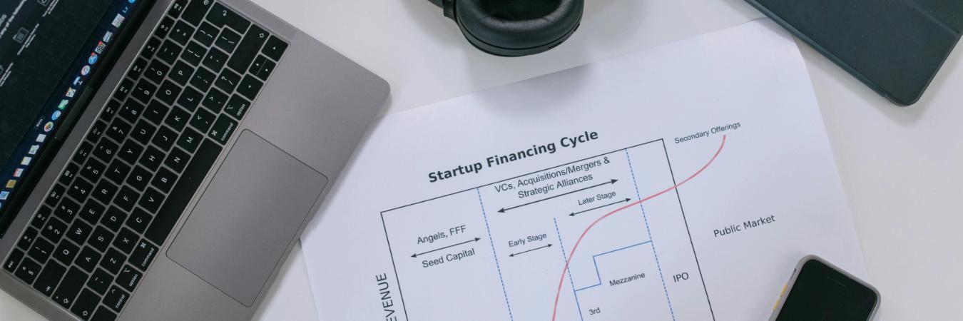 Flat lay of a modern workspace with tech gadgets and a startup financing cycle chart