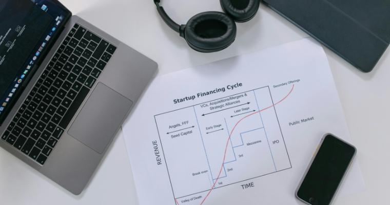 Flat lay of a modern workspace with tech gadgets and a startup financing cycle chart image link to article
