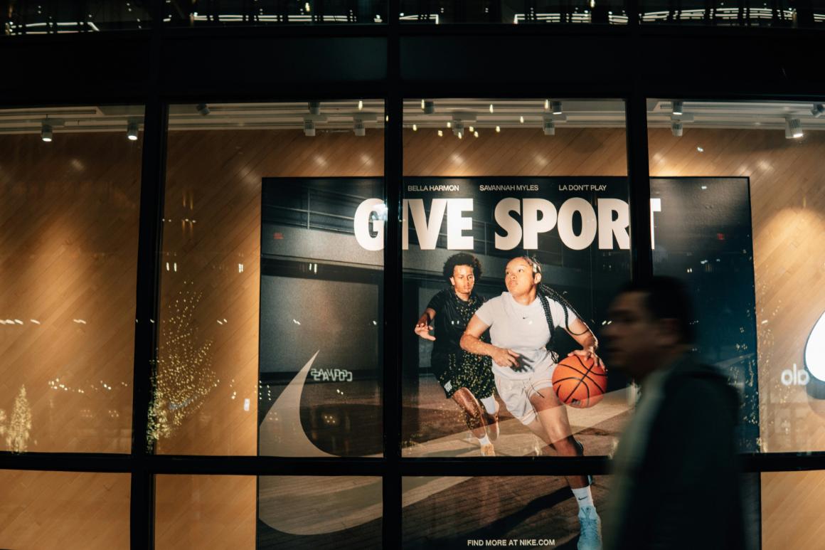 A vibrant Nike advertisement features two young basketball players, one male in a dark jersey and one female dribbling a basketball in a light gray outfit, with the slogan GIVE SPORT in bold white letters above them.
