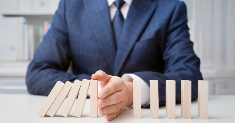 Person in a navy suit uses a hand to stop a row of wooden blocks from falling.