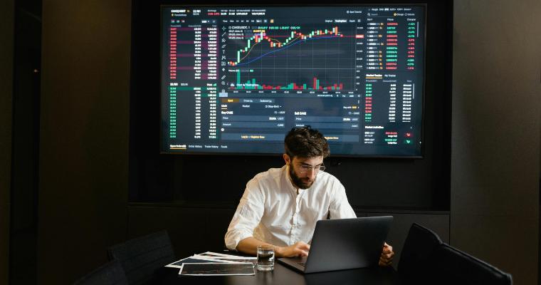 Economist working on laptop with graphs in background