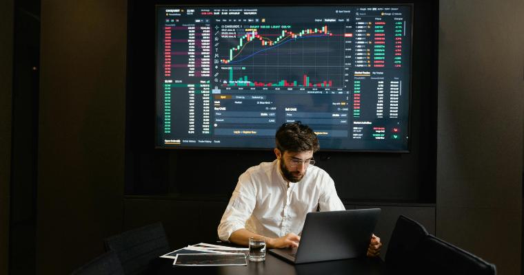 Economist working on laptop with graphs in background