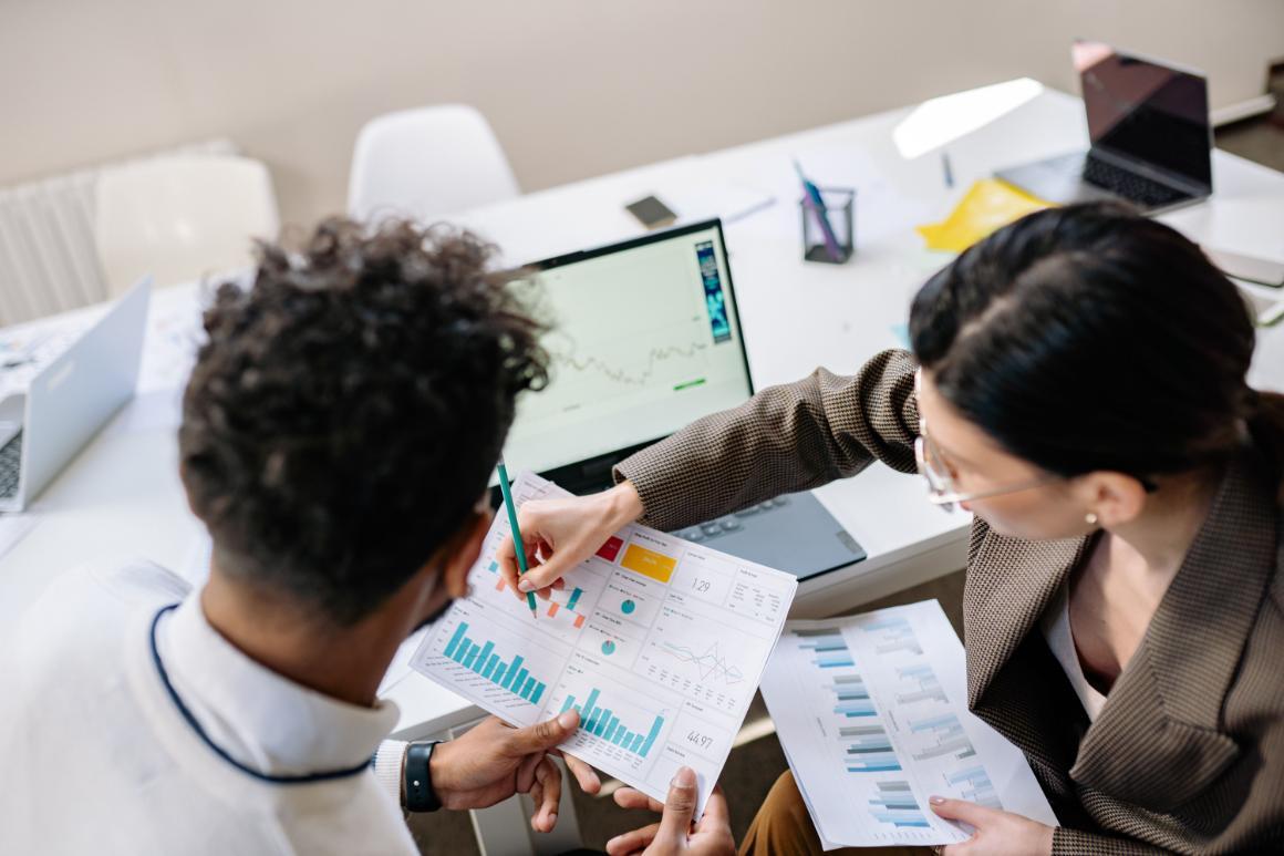 Two colleagues review printed charts and graphs around a conference table.