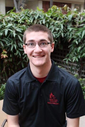 A person smiling in front of green foliage. Title: Eoin Lyons -- Net Impact.