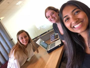 Three people smiling together at a desk in 'ACE Buddy Program'.