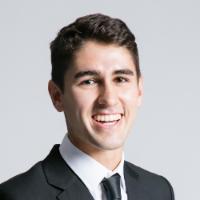 A man in a suit smiling against a plain background.