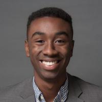 A person in a gray blazer smiling against a gray background.
