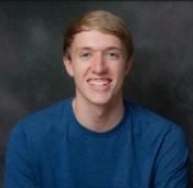A person in a blue shirt smiling against a dark background.