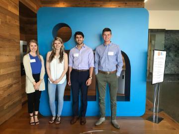 Four people posing by a blue wall during a company tour.