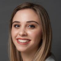 Young woman in a light blazer smiling against a gray background.