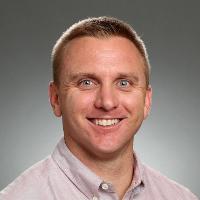 A person smiling in front of a gray background.