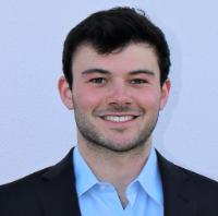 A person in a suit smiling against a plain background.