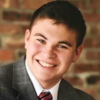 A person in a suit smiling against a brick background.