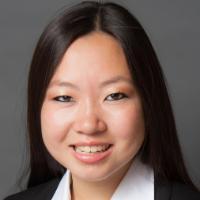 A person in business attire smiling against a gray background.