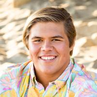 A person smiling outdoors wearing a colorful button-up shirt.
