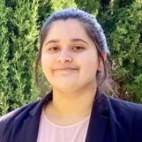A person with a blazer standing outdoors with trees in the background.