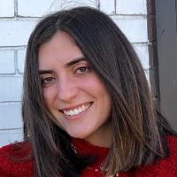 A person smiling in front of a white brick wall.