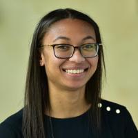 A person smiling, wearing glasses and a dark shirt.