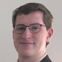 A person wearing glasses and a suit, smiling.